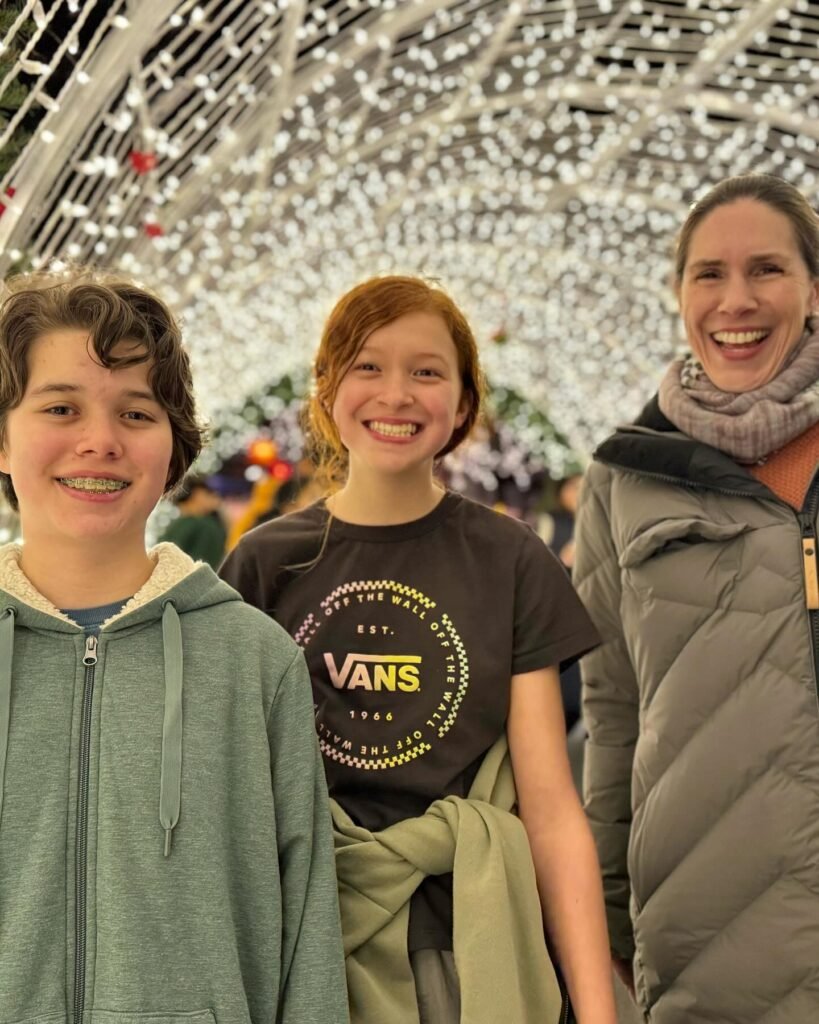 A smiling group stands beneath a canopy of white holiday lights, capturing the warmth of seasonal festivities.