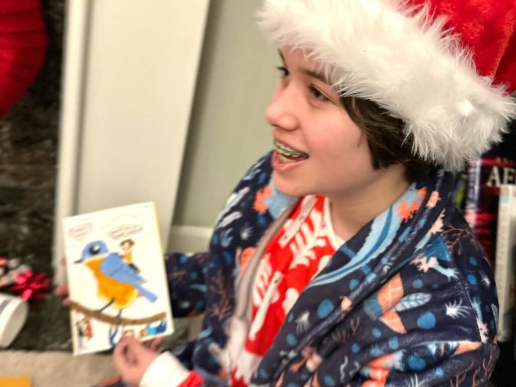A person wearing a festive Santa hat and pajama robe holds a card featuring a cardinals and a bluebird.