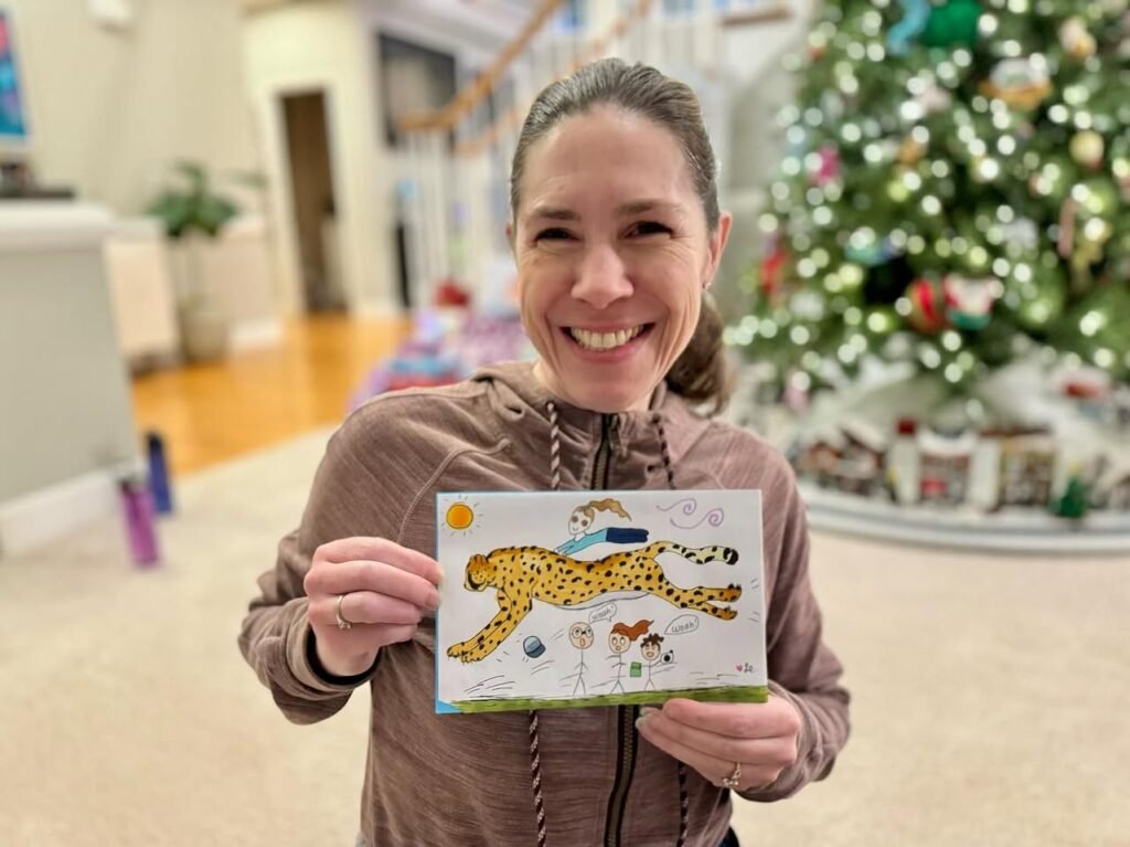 A person holds up a postcard featuring a cheetah illustration in front of a brightly lit Christmas tree.