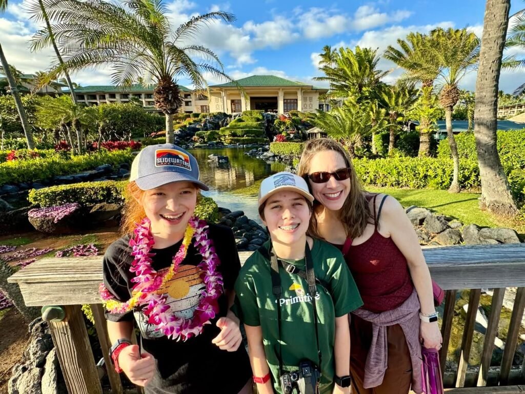 A family poses together on a tropical resort bridge surrounded by palm trees and a pond.