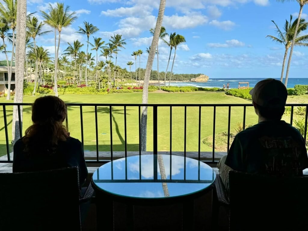 Relaxing on a balcony with a stunning view of palm trees and the ocean under a blue sky.