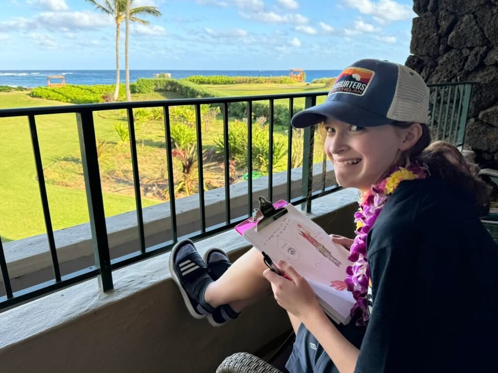 A person relaxes on a balcony overlooking a lush tropical landscape with palm trees and ocean views.