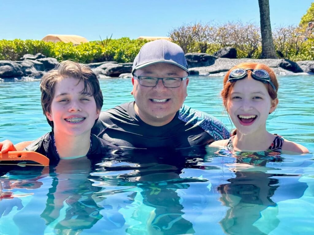A family enjoying a sunny day in a clear, turquoise water feature set against lush tropical greenery.
