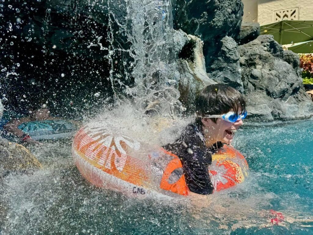 A person riding an inflatable tube during a splashdown at a water park, wearing goggles and laughing in excitement.
