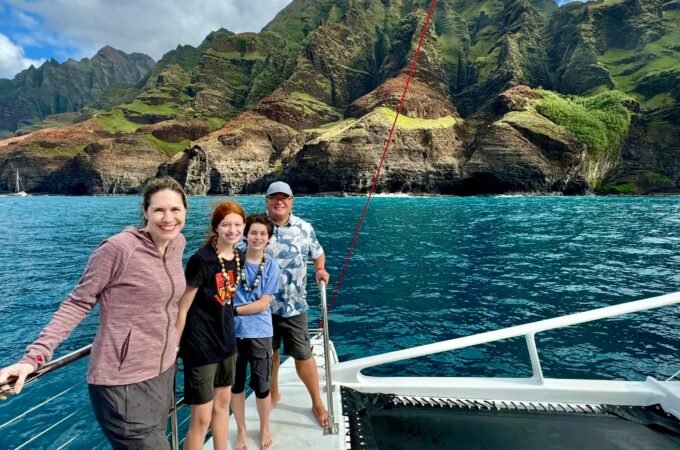 A family enjoying a catamaran vacation with a dramatic mountainous coastline in the background.