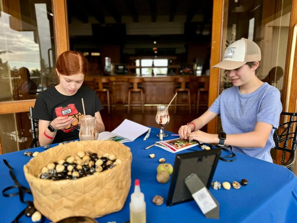 People at a craft table demonstrating non-slip mat design for river stones. A woven basket containing black and white stones sits on the blue tablecloth.