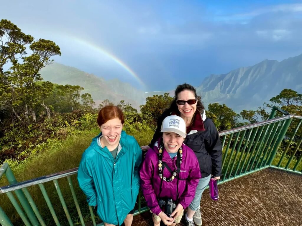 A family enjoys a scenic view of a rainbow over misty mountains from a lookout point in Monteverde Cloud Forest.