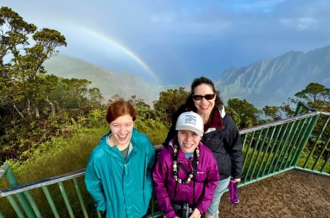 A family enjoys a scenic view of a rainbow over misty mountains from a lookout point in Monteverde Cloud Forest.