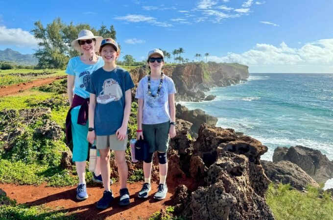 A group of people walking on a rocky coastal trail with ocean views and greenery.