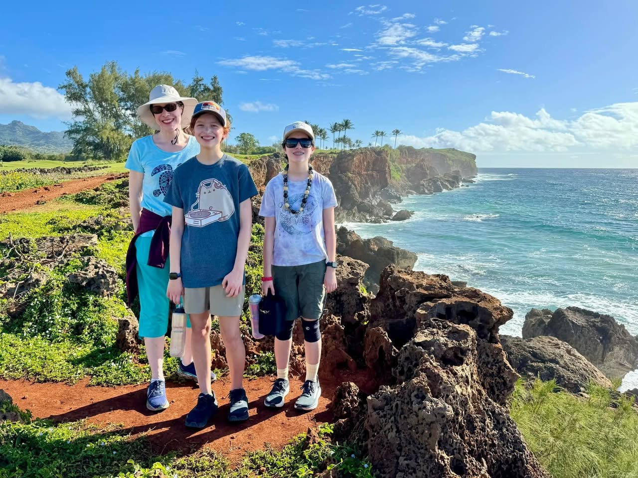 A group of people walking on a rocky coastal trail with ocean views and greenery.