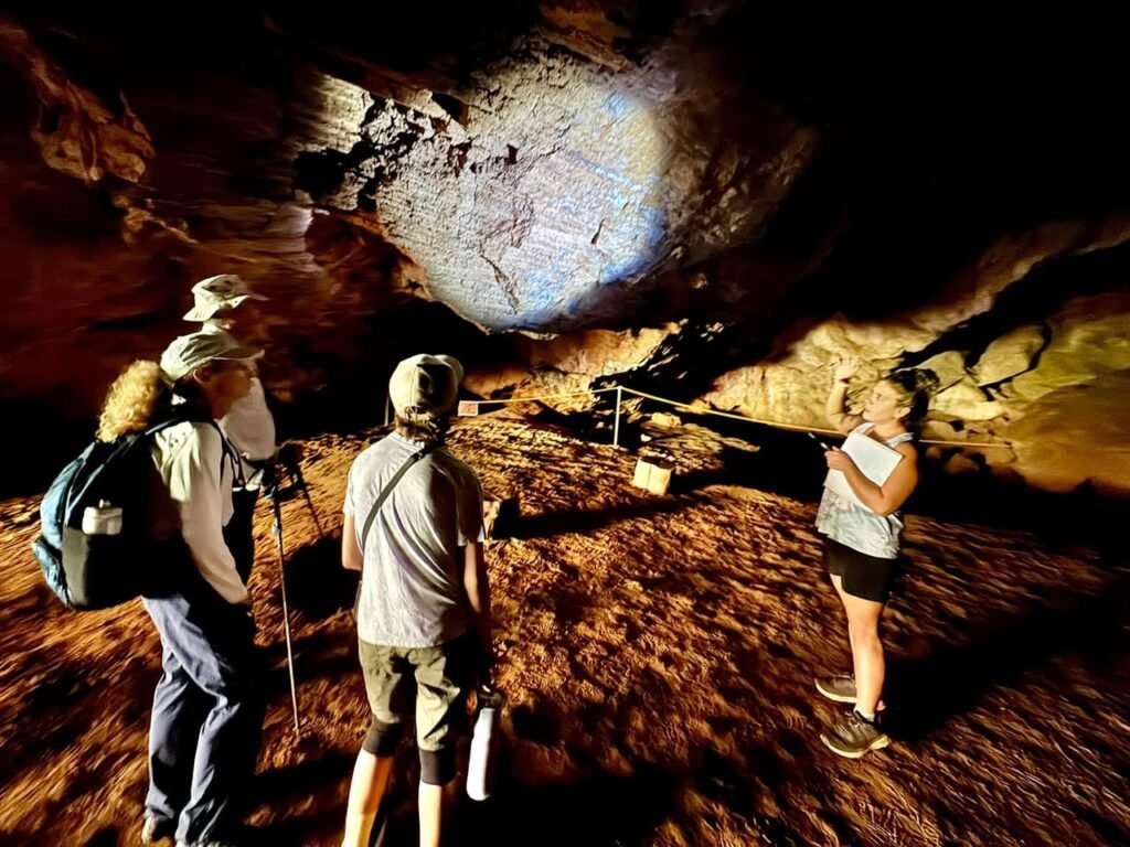 A group of hikers explores a rocky cave with textured walls illuminated by natural light.
