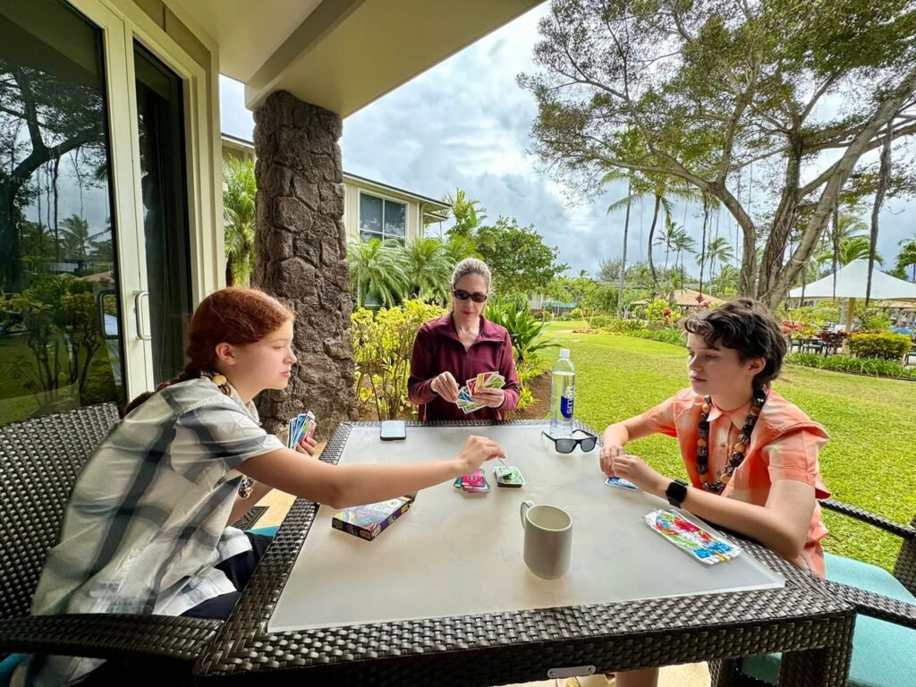 People enjoying a board game on a patio overlooking lush tropical gardens and palm trees.