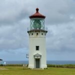 Eating Kauai A white lighthouse with a red roof standing near the sea under a cloudy sky. Close up details of the lighthouse lens and a patio area.