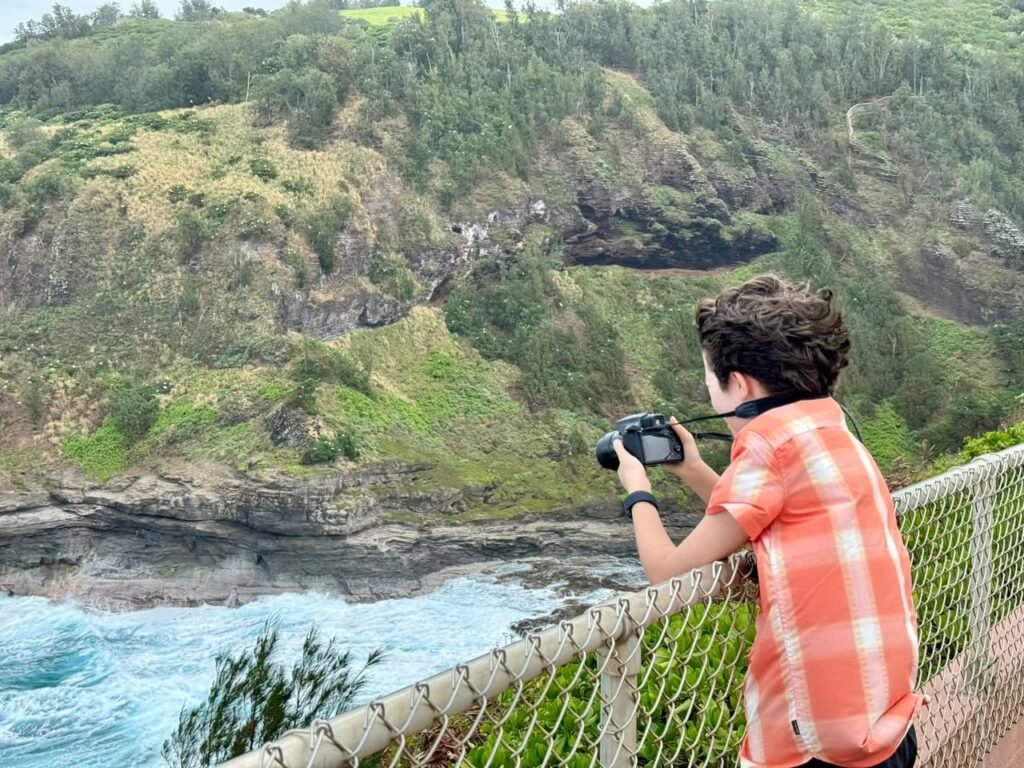 A person in an orange plaid shirt photographs a tidepool on a rocky coastal bluff.