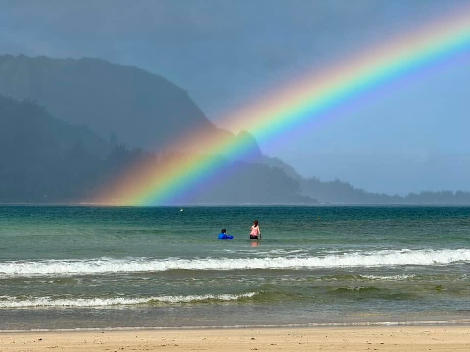 A magical double rainbow arches gracefully over a calm Pacific Northwest beach.