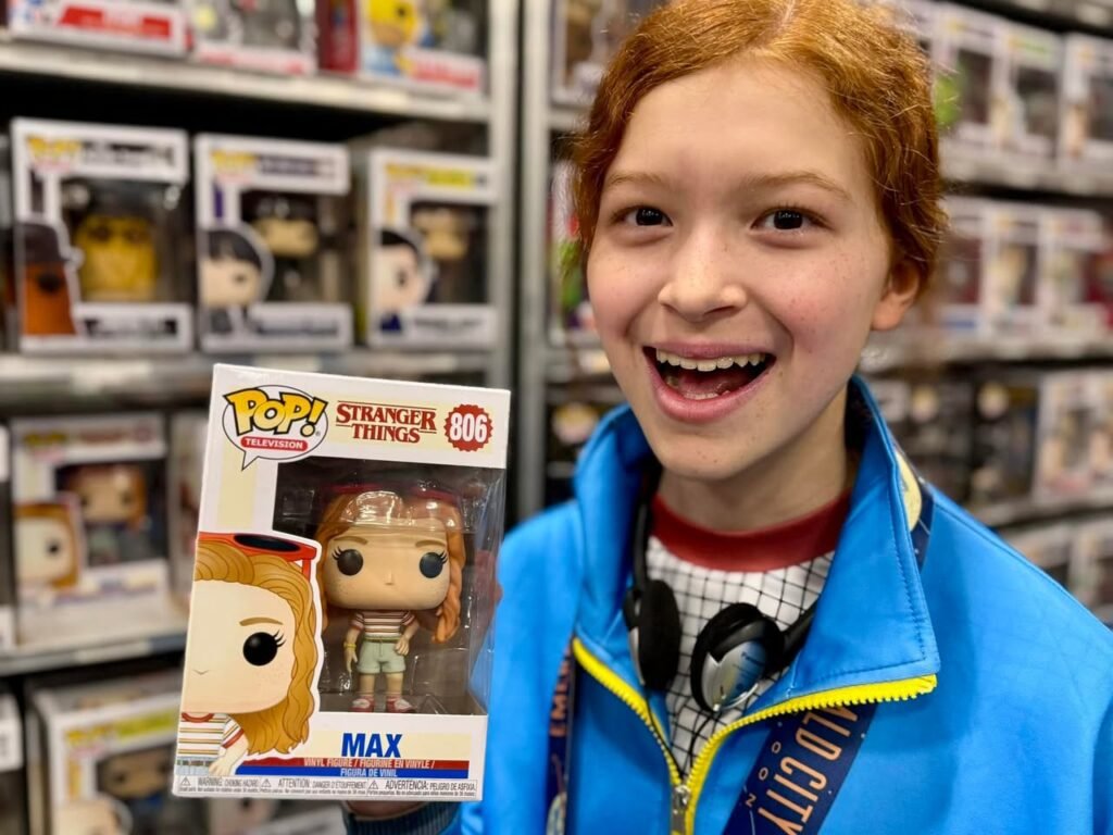 A person grins while holding a Stranger Things Max Funko Pop figure in a retail setting.