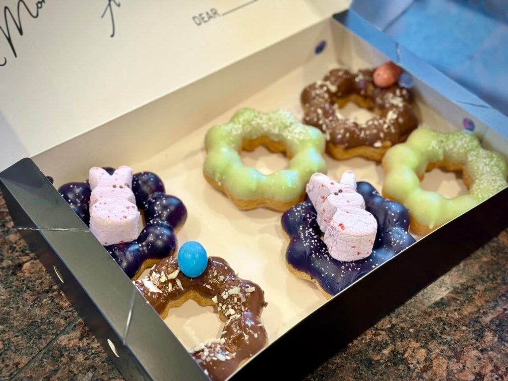 A box of colorful Easter-themed donuts, sprinkled icing, and bunny decorations.