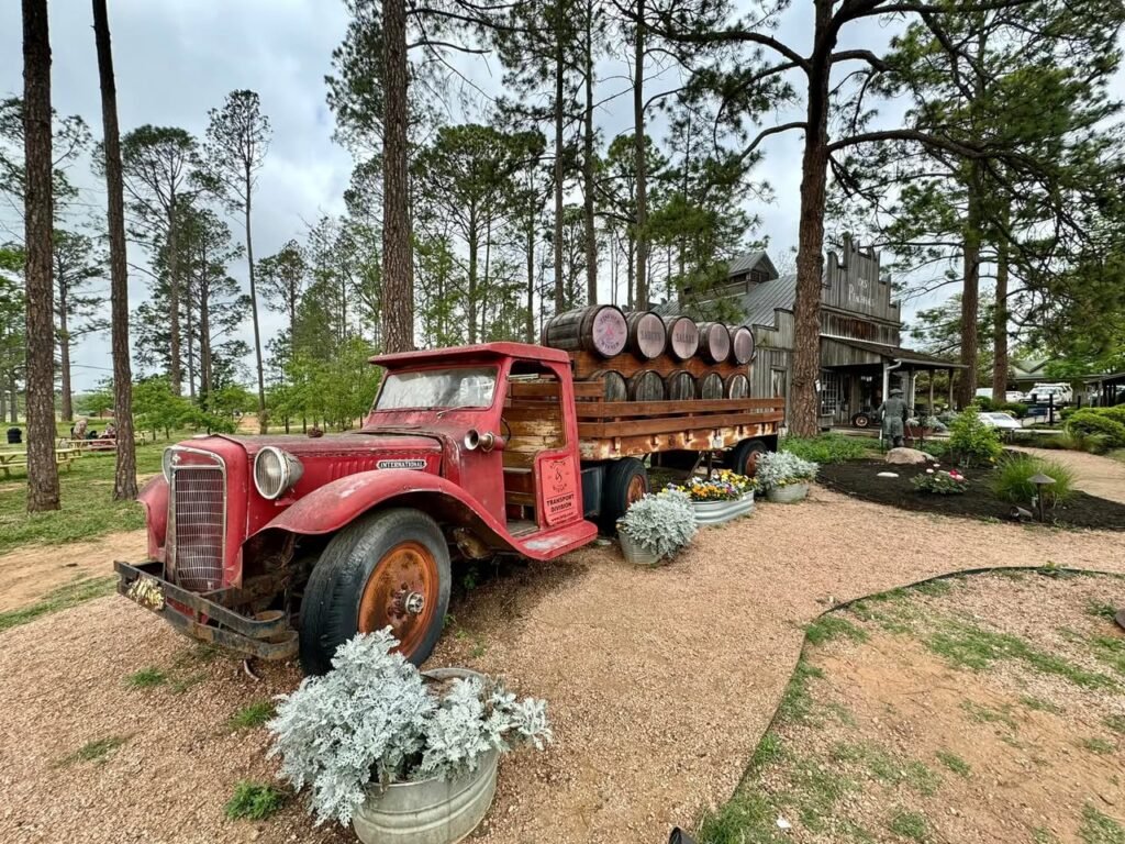 A vintage red truck loaded with logs in a pine forest. Tall trees and rustic decor create a nostalgic atmosphere.