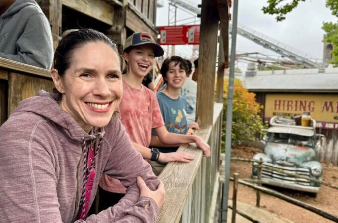 A family enjoys a day at an amusement park, watching the rides and attractions from a wooden stand.