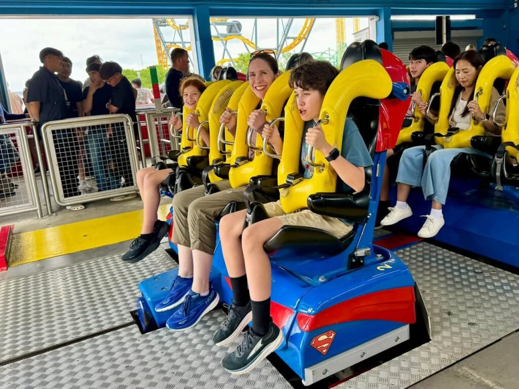 A group of people seated in a roller coaster car, secured with yellow restraints, at an amusement park.