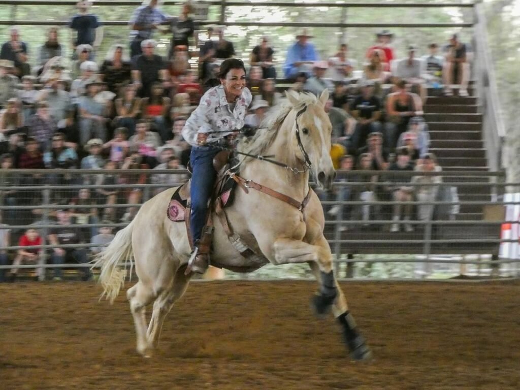 A rider on a white horse galloping in an arena with an audience watching.