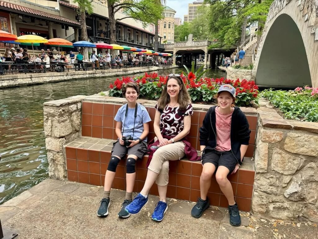 A family enjoys a relaxing moment at a scenic canal in Disney Springs, surrounded by colorful umbrellas and vibrant flowers.