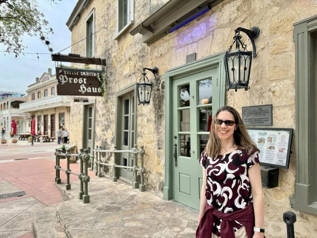 A visitor stands in front of the historic stone facade of Le Petit Train Ghost House, with a close-up detail of the hanging wooden sign visible.