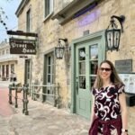 Historic Market Square A visitor stands in front of the historic stone facade of Le Petit Train Ghost House, with a close-up detail of the hanging wooden sign visible.