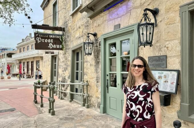 A visitor stands in front of the historic stone facade of Le Petit Train Ghost House, with a close-up detail of the hanging wooden sign visible.