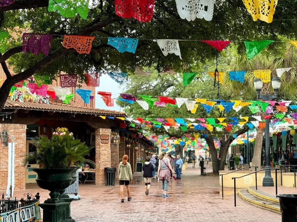 Vibrant banners and flags stretch across a brick walkway and frame a large garden urn.
