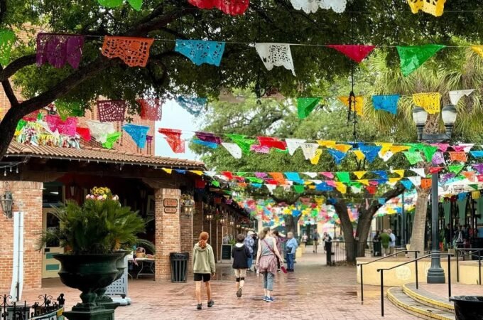 Vibrant banners and flags stretch across a brick walkway and frame a large garden urn.