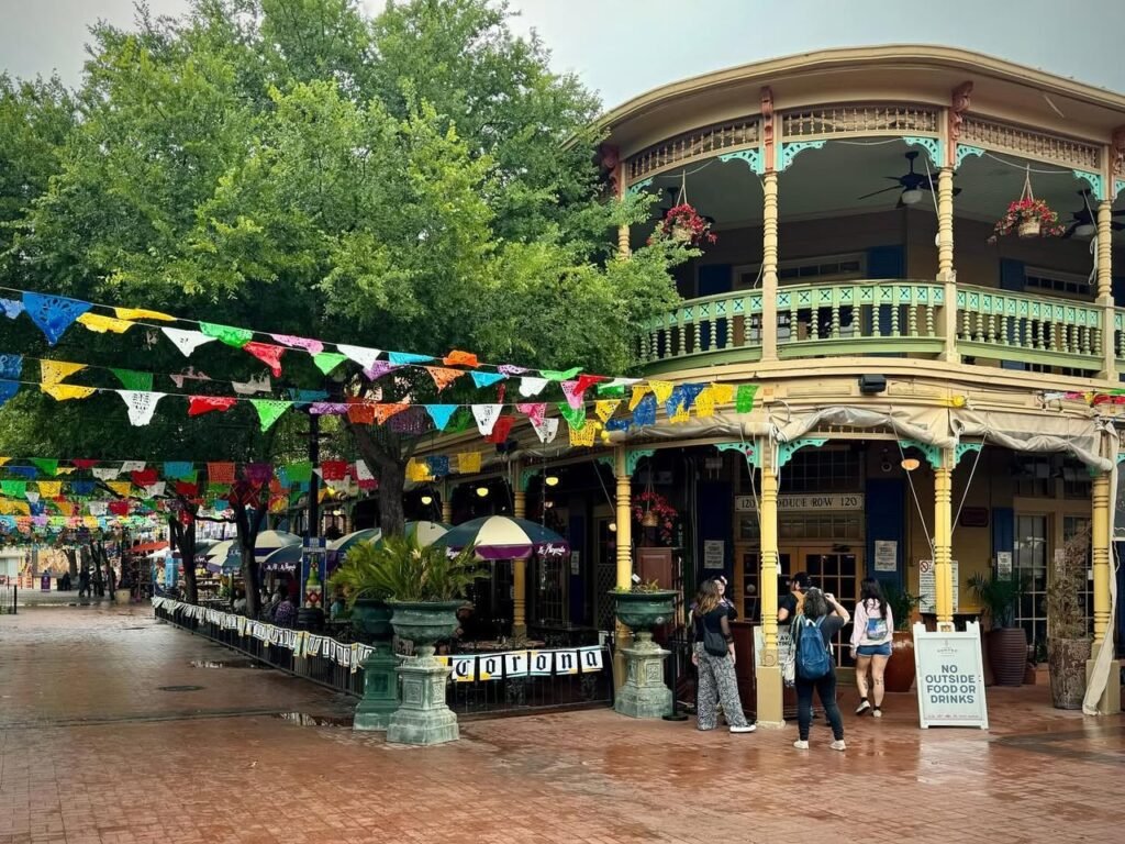 A historical two-story pavilion with colorful bunting hanging from trees and a large building.