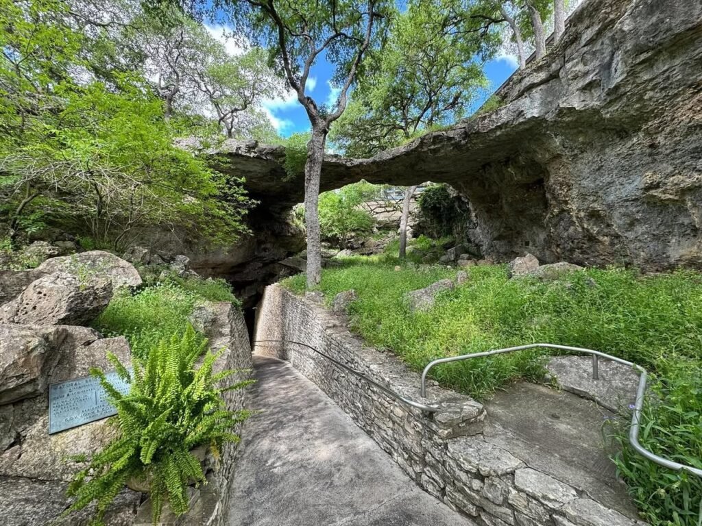 A scenic outdoor path featuring natural rock formations, lush green plants, and stone walls. The area highlights unique geological features and well-maintained hiking trails.