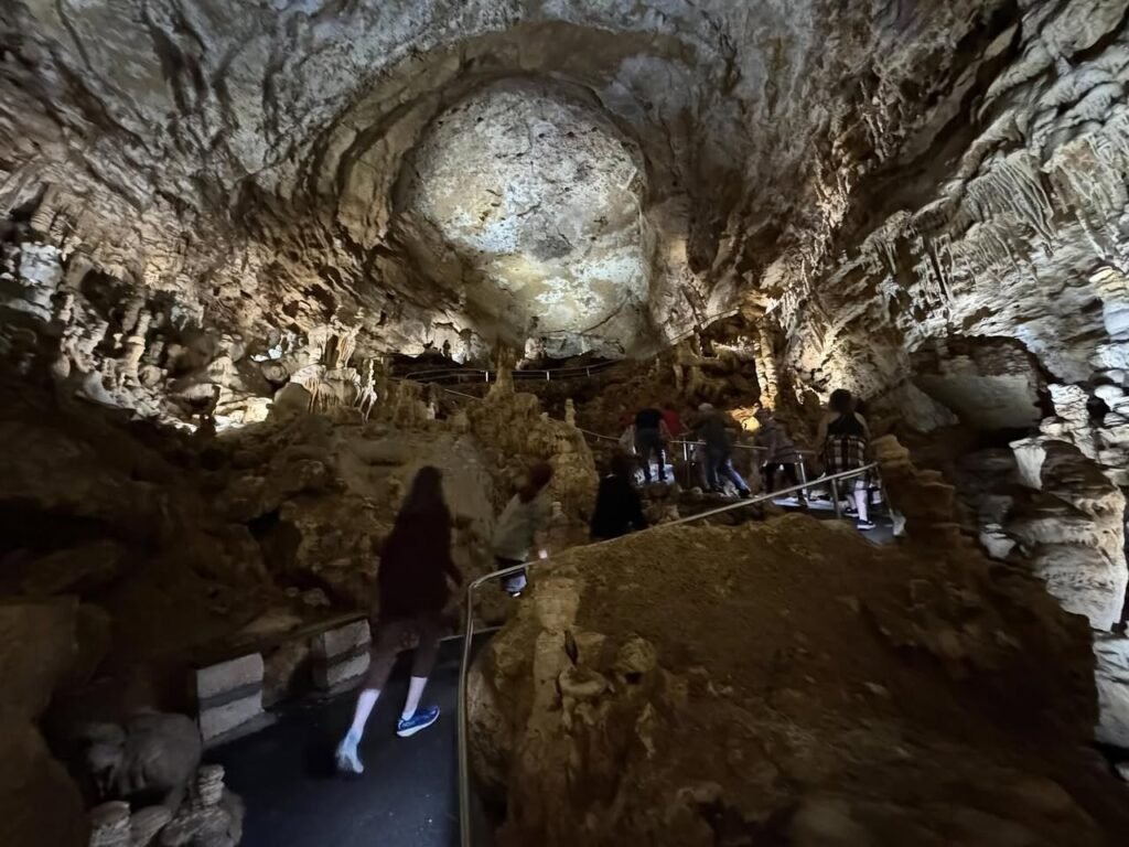 Visitors navigating a walkway through a vast limestone cavern with dramatic ceiling formations.