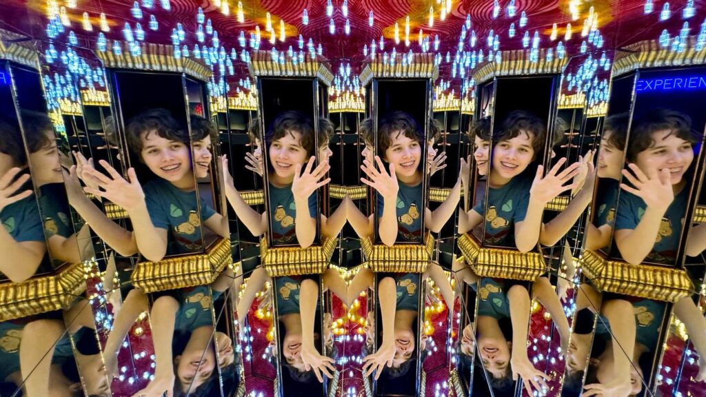A fun photo of a young visitor waving in a multicolored mirror maze.