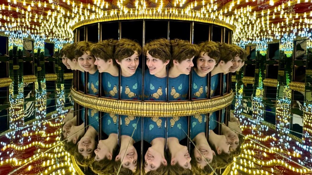 Visitor exploring a circular funhouse mirror corridor packed with dazzling lights.