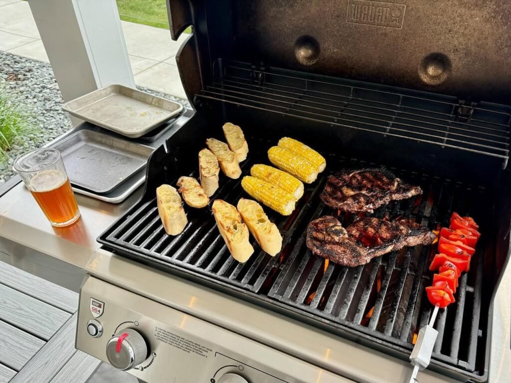 A gas grill covered with corn on the cob, ribs, and peppers.
