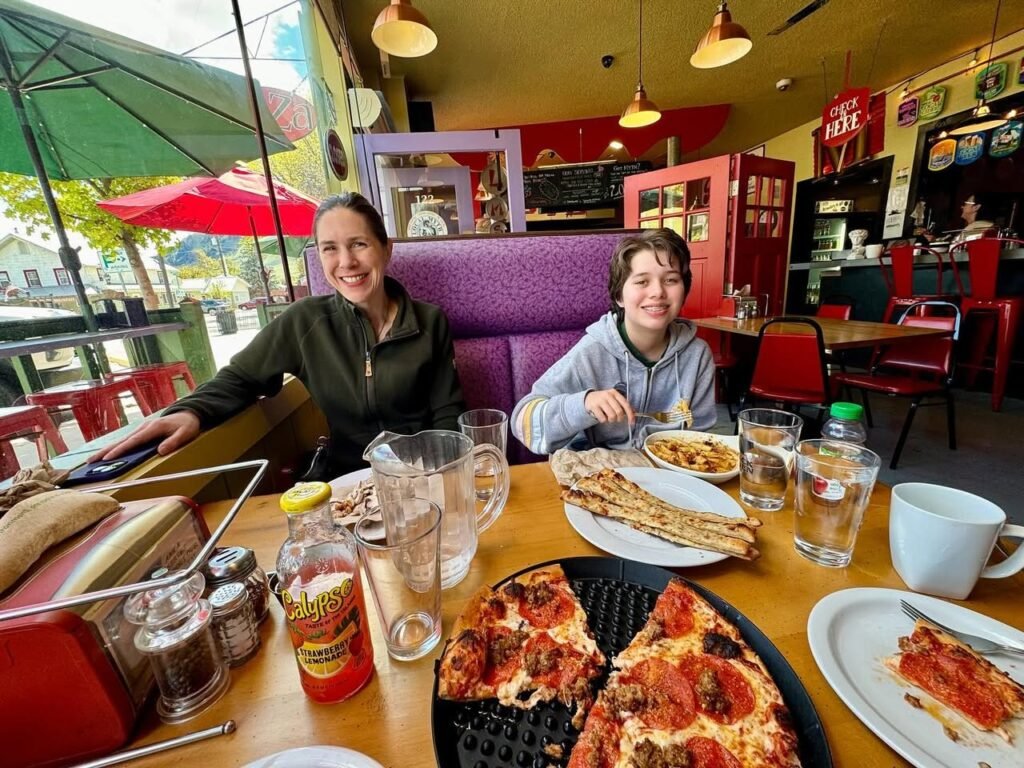 Diners sharing a meal of pizza and a panini sandwich at a colorful restaurant.