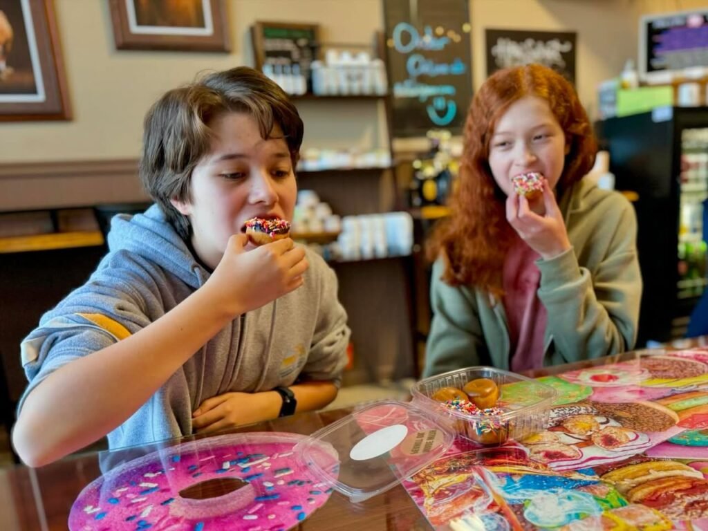 Two individuals enjoying decorated donuts at a table in a cozy donut shop setting.