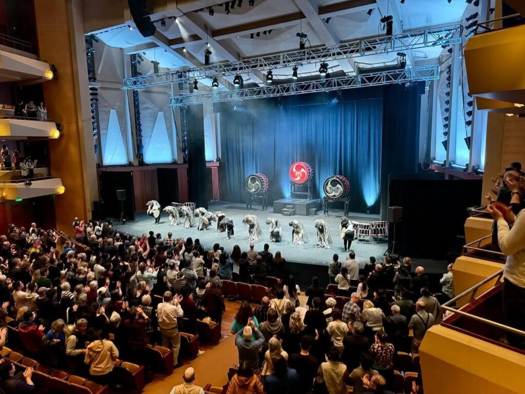 A Polish circus performance featuring white horses and performers on a stage with a blue curtain and red light at the Polish Cultural Center in Seattle