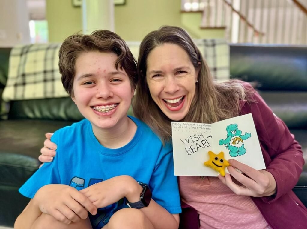 Two happiest-looking people on a couch sharing a handmade card that says Wish Bear. There's a colorful cartoon bear on the card.