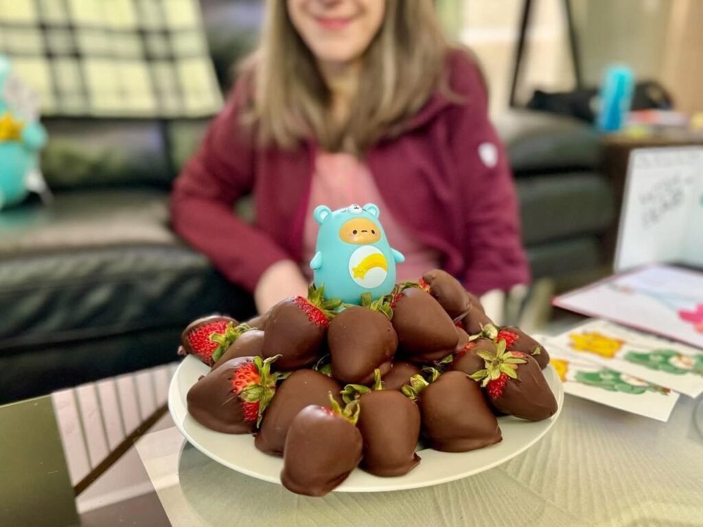 A plate of chocolate-dipped strawberries is shared in a cozy living room with Easter-themed cards nearby.