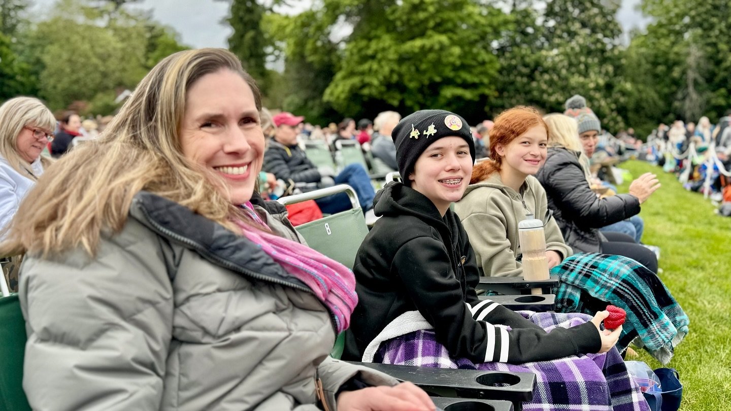 Sarah McLachlan with Feist A family of four sits together on green stadium seats at an outdoor cultural gathering, smiling warmly against a backdrop of lush trees.