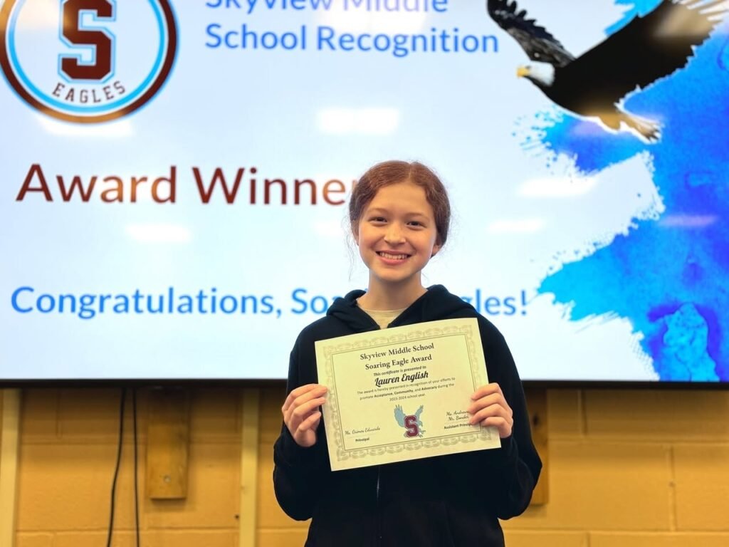 A smiling student proudly presents a Skyview Middle School award in front of a congratulatory banner.