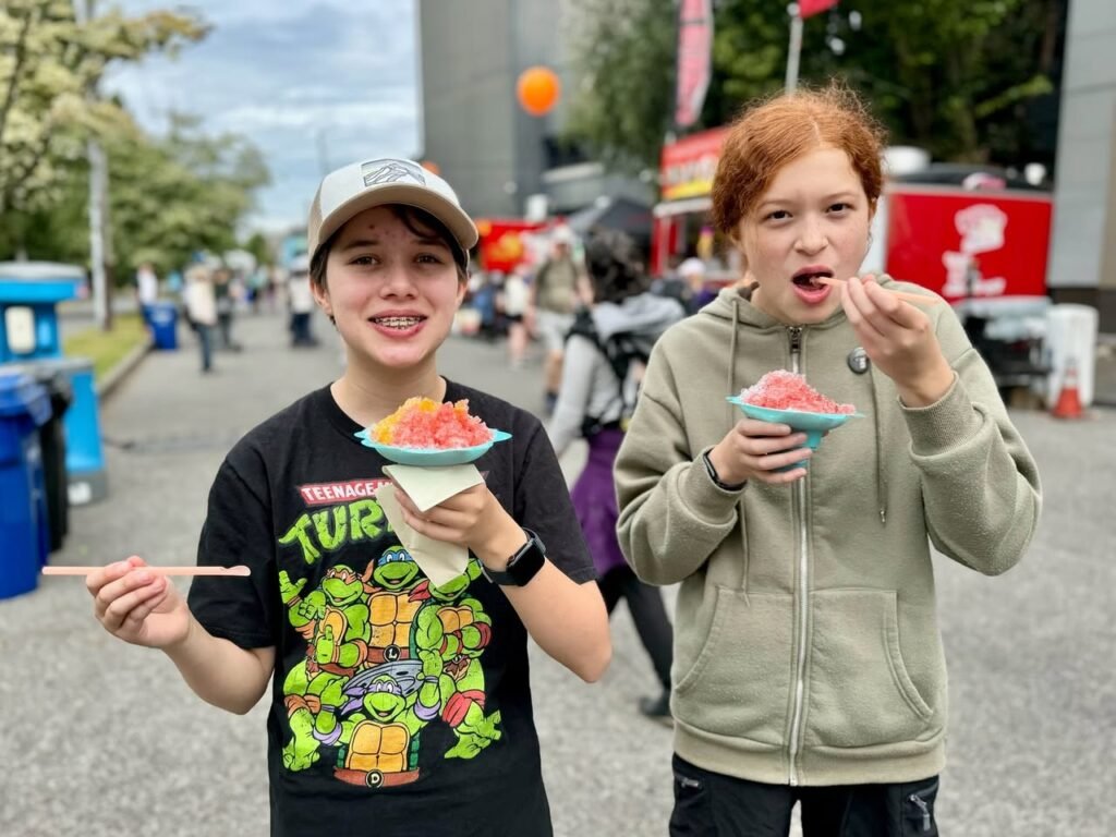 Two people enjoying shaved ice during a lively outdoor street event.