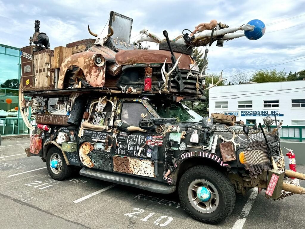 A creatively modified apocalypse-themed vehicle covered in scrap metal and antlers. The car features a blue sphere on an extended pole.