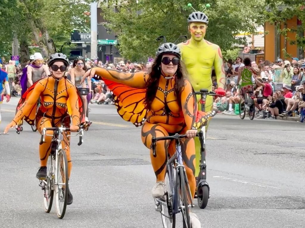 Bicyclists dressed as monarch butterflies ride through a crowded urban street during a festival event.