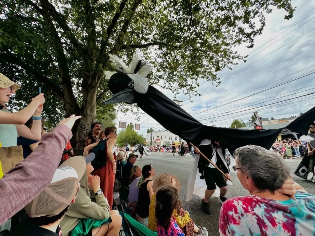 Crowd watches a parade featuring a large black-and-white costume under leafy trees.