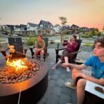 A family sits around a circular outdoor fire pit at sunset, s'mores on hand.
