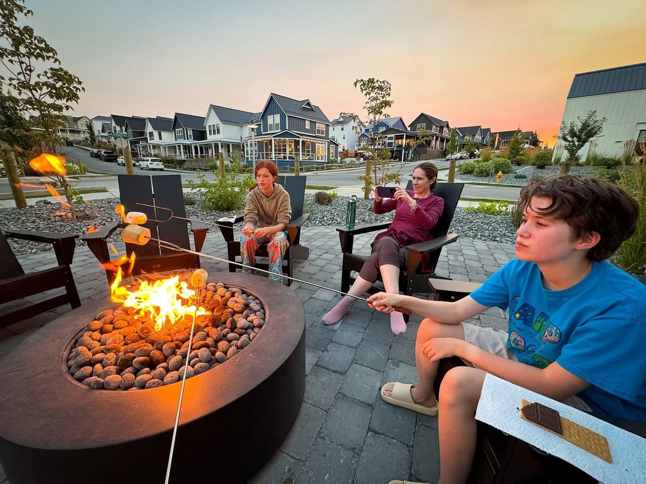 S’mores A family sits around a circular outdoor fire pit at sunset, s'mores on hand.
